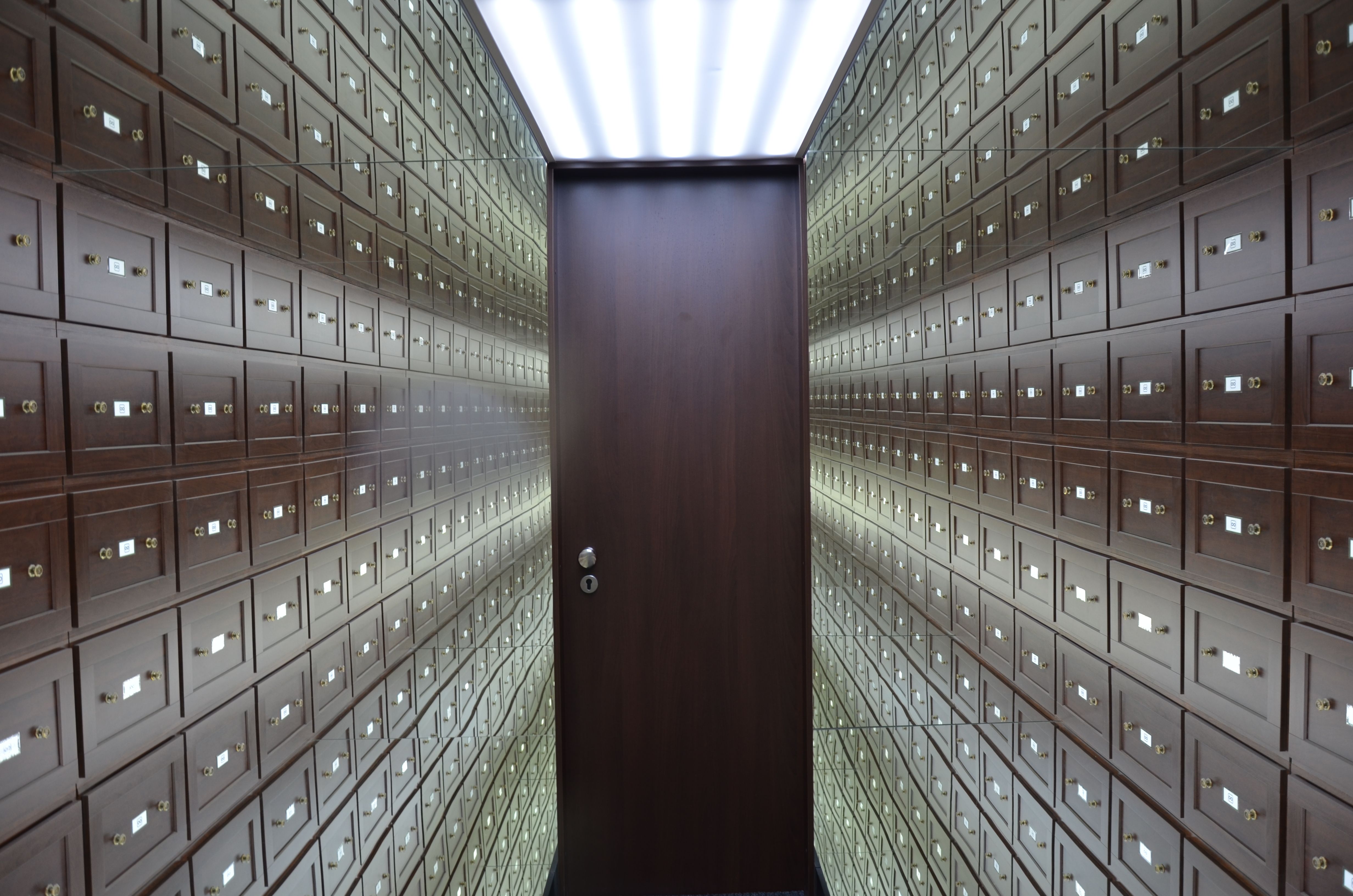 Wooden lockboxes line the walls of a modern, secure vault with a central wooden door